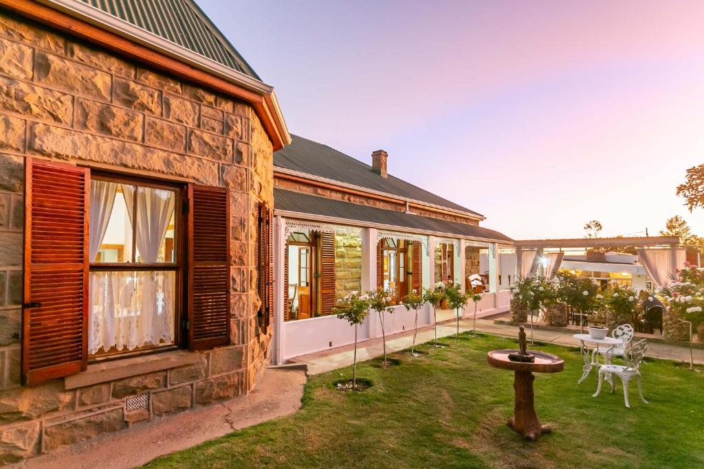 a stone house with a courtyard with a table and chairs at Ravenscliff Manor in Oudtshoorn