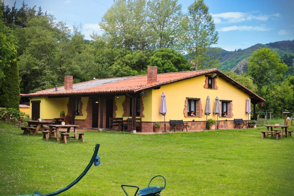a yellow house with picnic tables in the grass at Apartamentos Rurales El Buxu in Soto de Cangas
