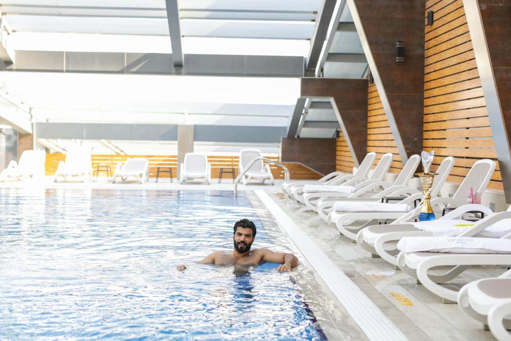 un uomo che nuota in una piscina con sedie di VIP Hotel Doha Qatar a Doha