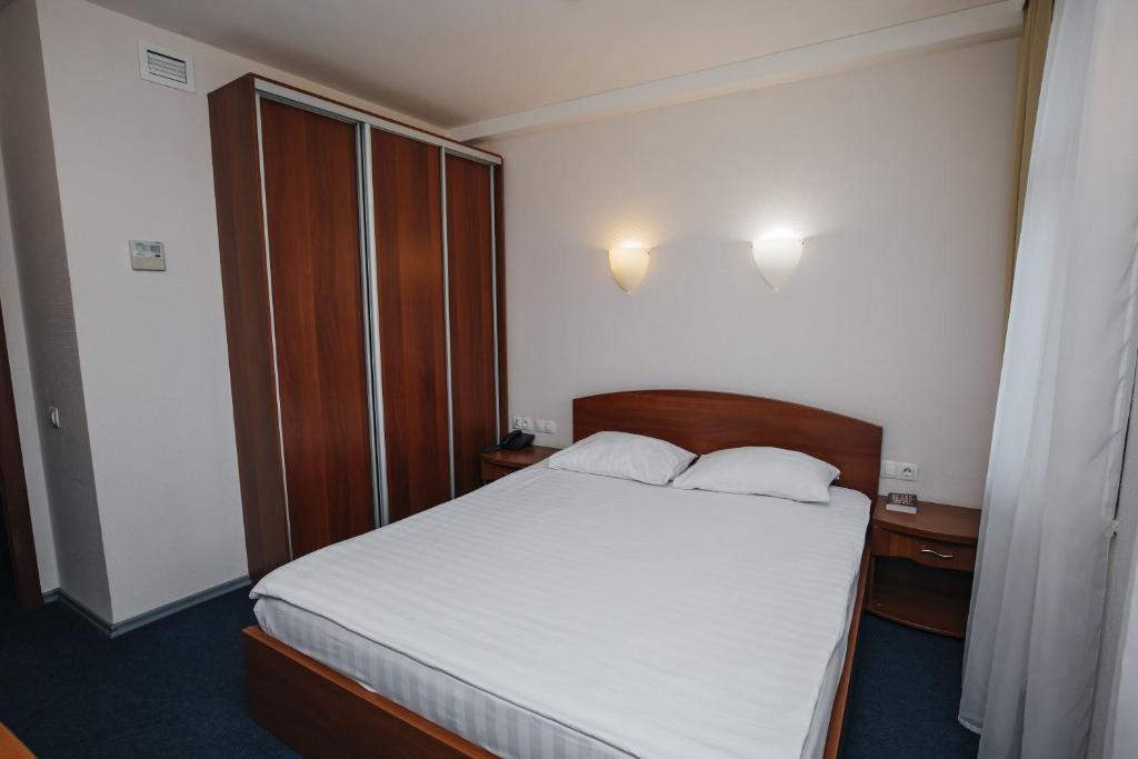 a bedroom with a bed with white sheets and wooden furniture at Emerald Hotel in Yekaterinburg