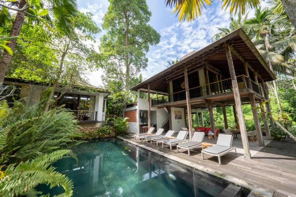 a house in the jungle with a pool and lounge chairs at Surya Kembar Villas in Ubud