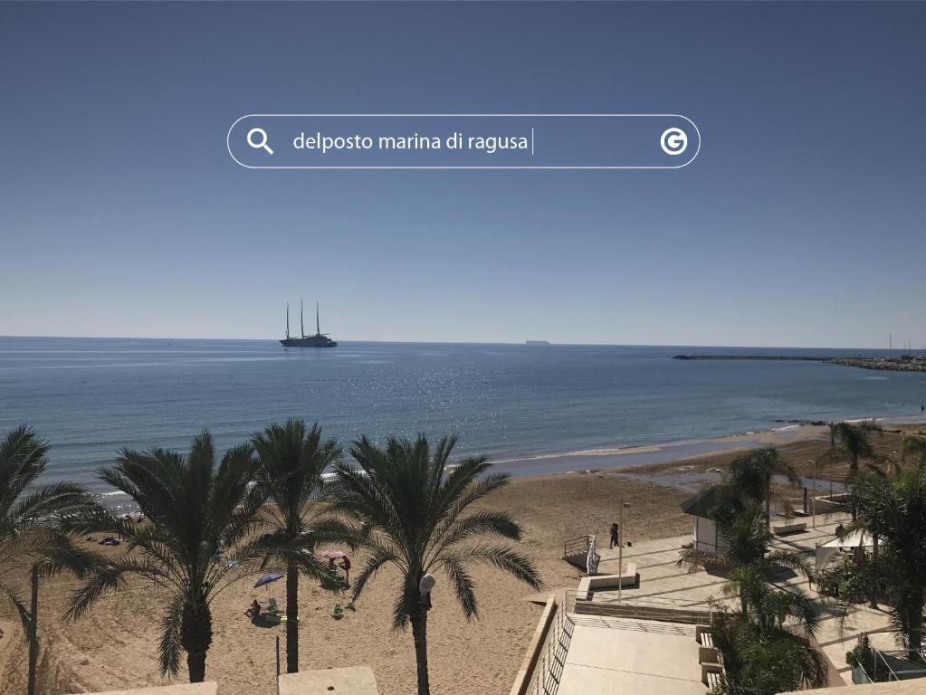 einen Strand mit Palmen und ein Schiff im Wasser in der Unterkunft DELPOSTO Marina di Ragusa (elt) in Marina di Ragusa