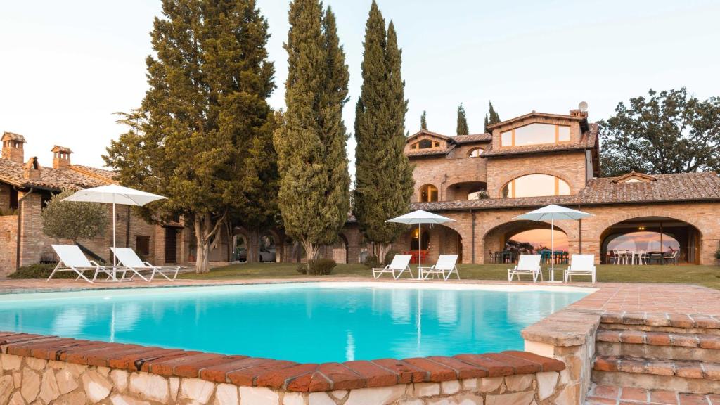 a pool in front of a house with chairs and umbrellas at Miataland in Collazzone