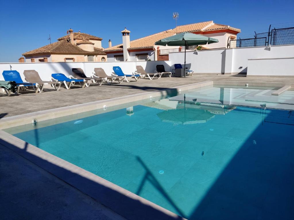 a swimming pool with chairs and an umbrella at A 15 minutos Granada piscina jacuzzi barbacoa in Güevéjar