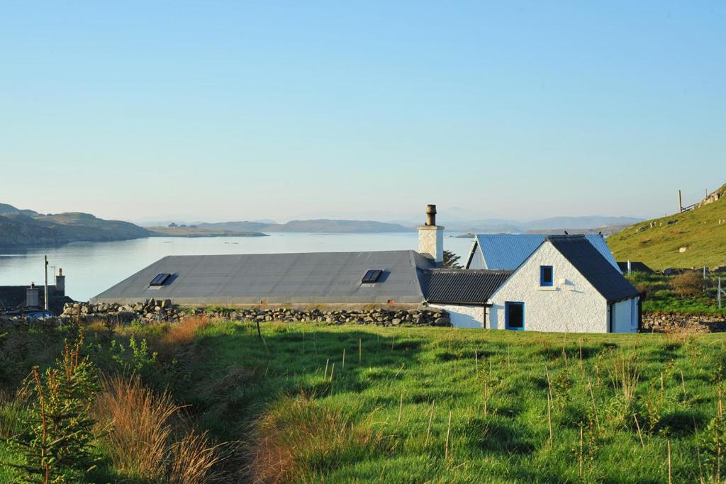 a house on a hill next to a body of water at Tigh Bhisa Blackhouse in Tolstachaolais