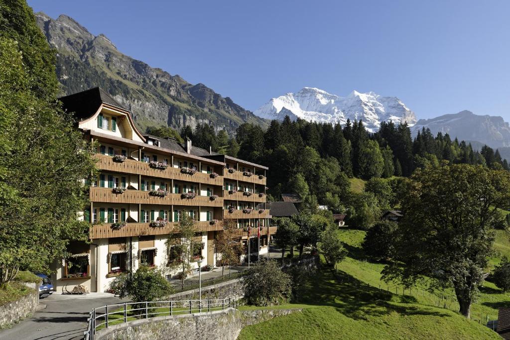 a hotel on a hill with mountains in the background at Hotel Alpenrose Wengen - bringing together tradition and modern comfort in Wengen