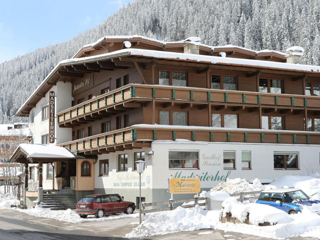 een groot gebouw met auto's geparkeerd in de sneeuw bij Gasthof Pension Madseiterhof in Tux