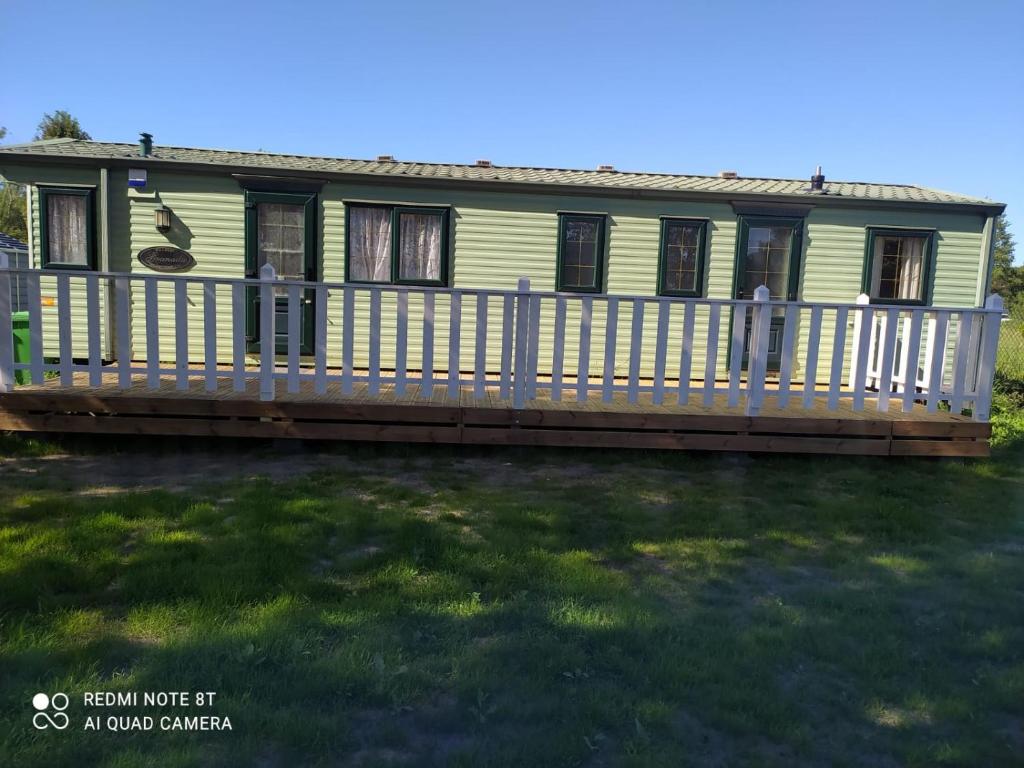 a green house with a porch and a deck at Karwia-Karwieńskie Błota domek przy plaży in Karwieńskie Błoto Drugie