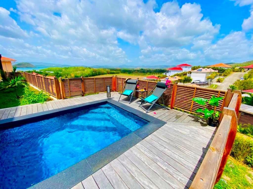 une piscine avec deux chaises et une terrasse en bois dans l'établissement Villa Passion Cannelle de standing avec sa piscine vue mer, à Les Trois-Îlets