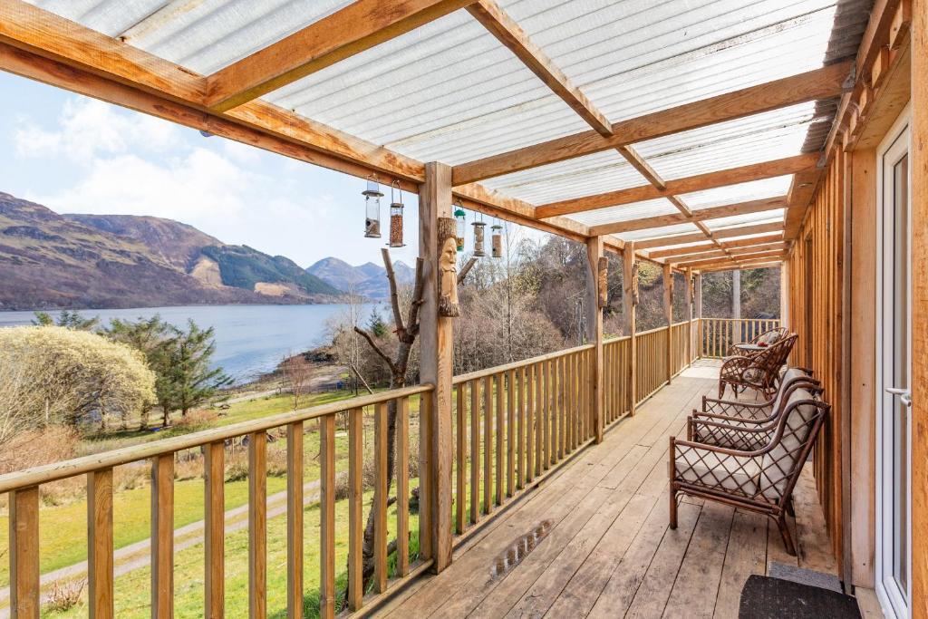 a wooden porch with chairs and a view of the water at Druidaig Cottage in Letterfearn