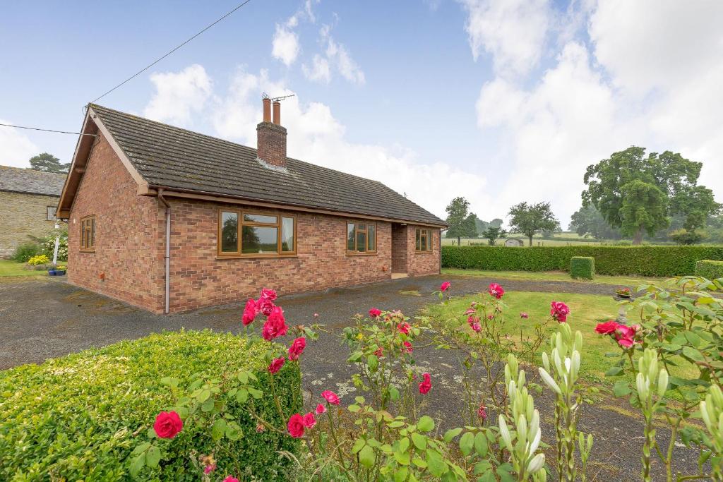 ein Backsteinhaus mit roten Blumen davor in der Unterkunft Meadow Lea in Leominster