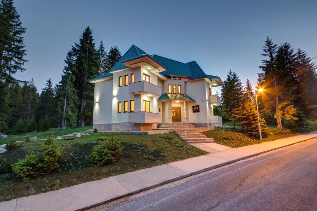 a large white house with a green roof on a street at Apartmani Bijelic in Žabljak