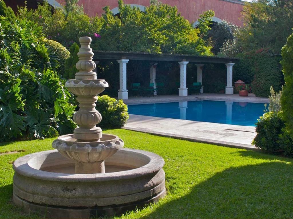 a stone fountain in the grass next to a swimming pool at Hotel Gobernador in Durango