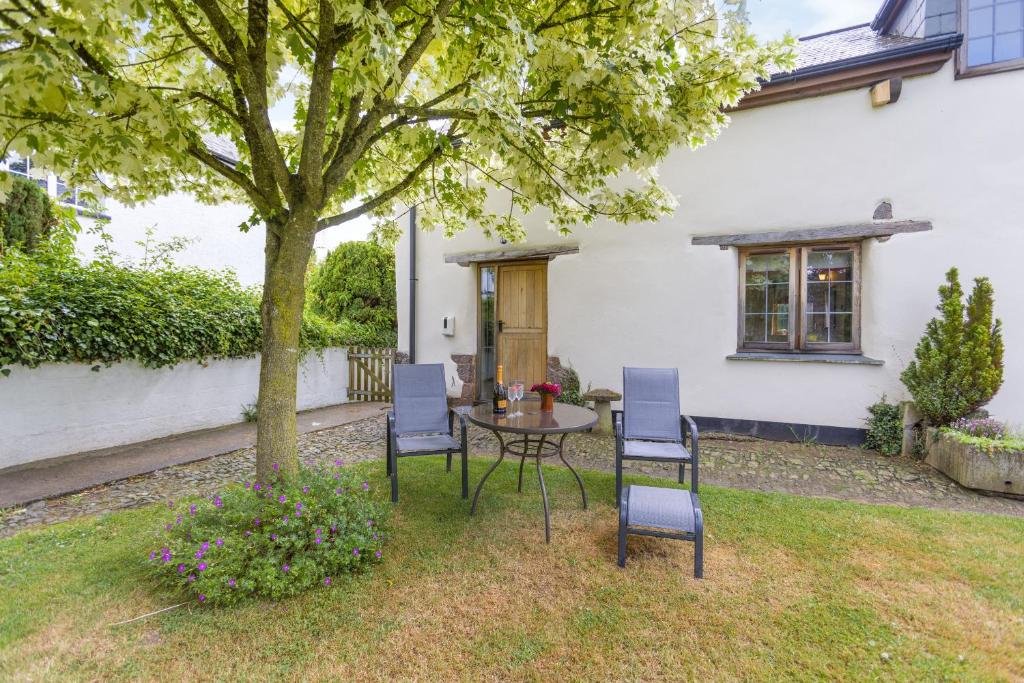 a patio with a table and chairs under a tree at The Yoke in Tedburn Saint Mary