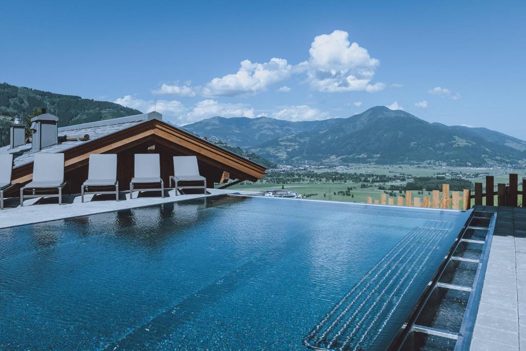 una piscina con sillas y montañas en el fondo en Bergdorf Hotel Zaglgut en Kaprun