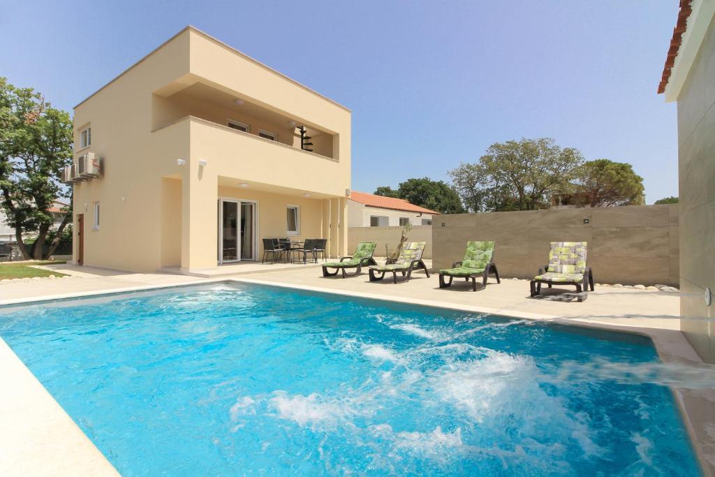 a swimming pool with chairs and a house at Villa Sunshine with private Hydromassage Pool near the beach in Peroj
