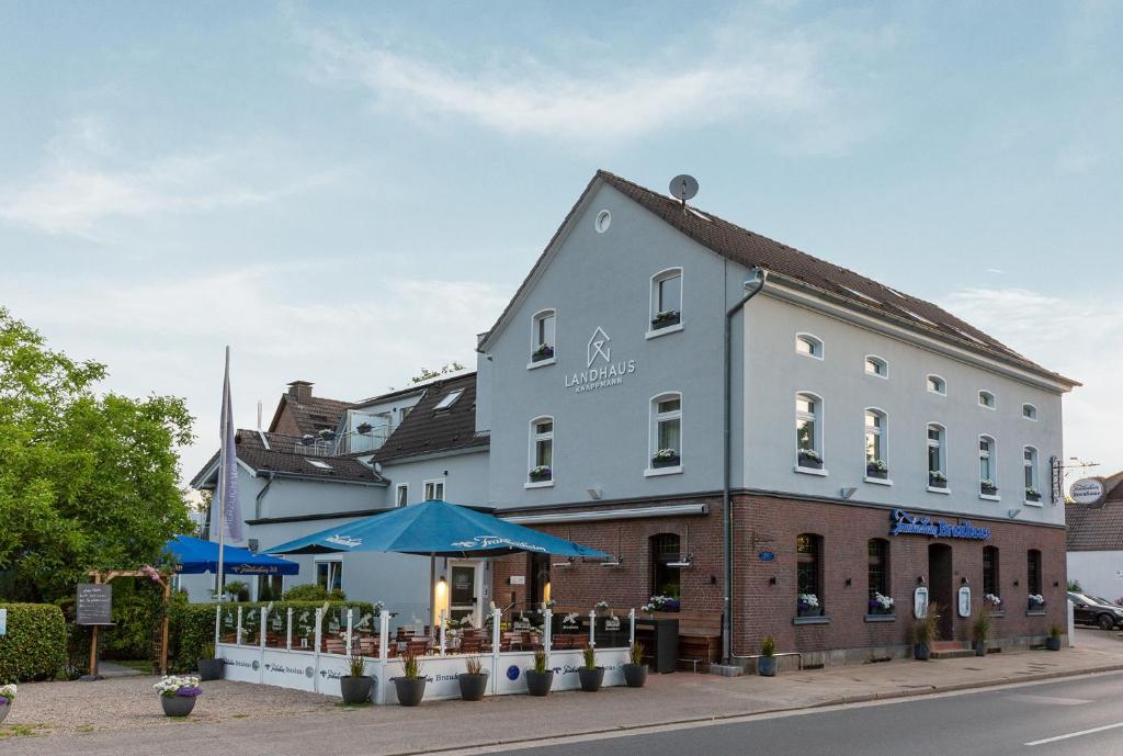 ein weißes Gebäude mit blauen Sonnenschirmen davor in der Unterkunft Hotel Landhaus Knappmann in Essen