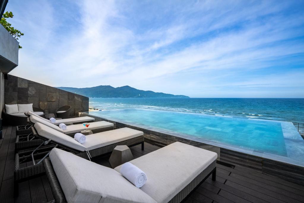 a swimming pool with chaise lounge chairs and the ocean at M SUITE Danang Beach in Da Nang