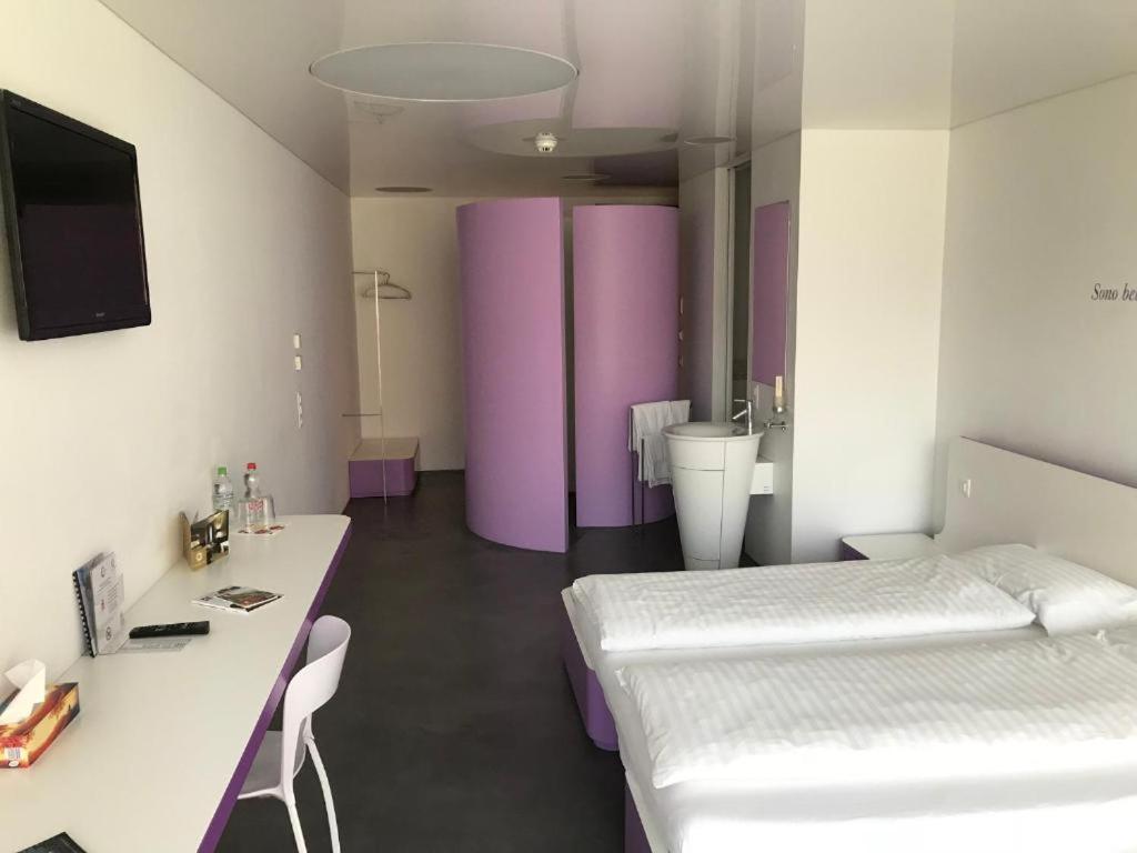 a room with two beds and a desk and purple walls at Chromotel self check-in in Mezzovico