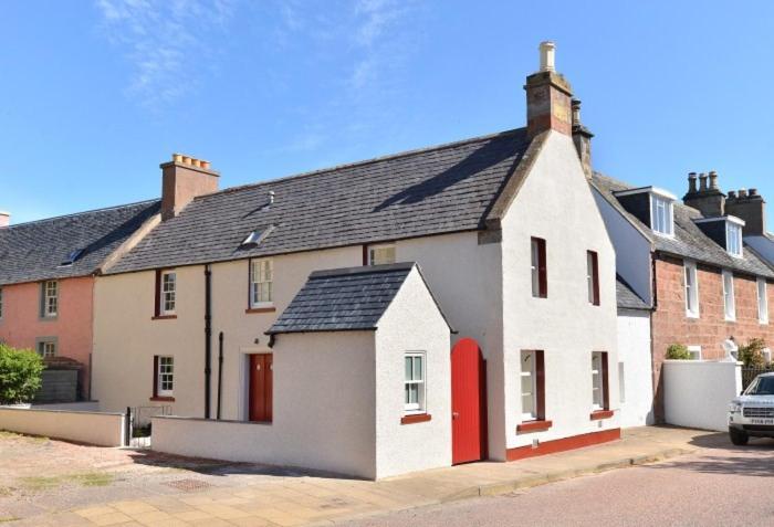 uma grande casa branca com uma porta vermelha em Seashell Cottage em Cromarty