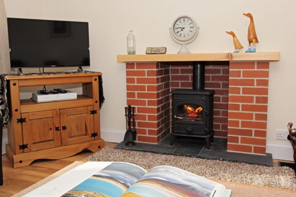 a living room with a brick fireplace and a tv at Old Post Office in Tarbert