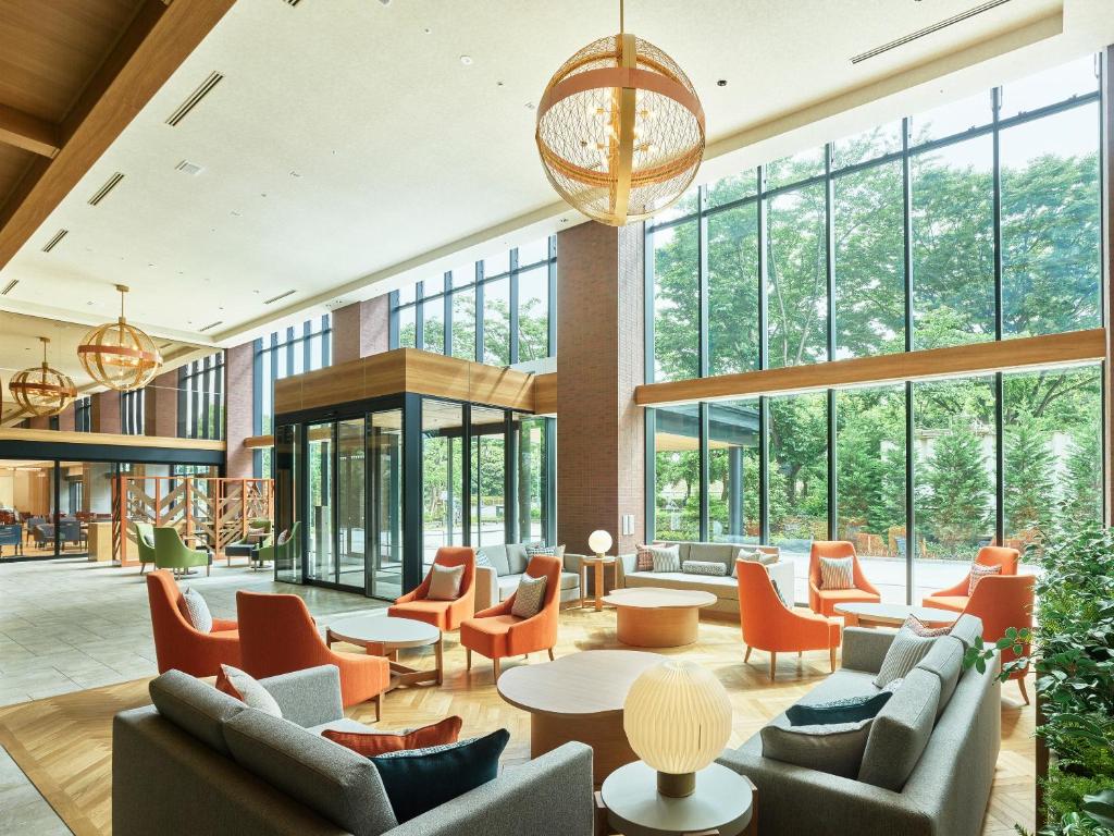 een lobby met stoelen en tafels en grote ramen bij Mitsui Garden Hotel Kashiwa-no-ha Park Side - Chiba in Kashiwa