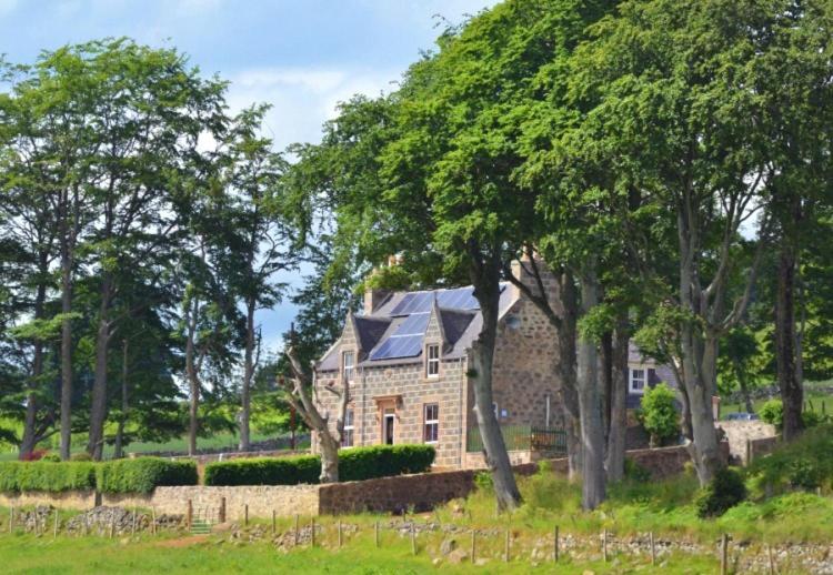 una casa de piedra con techo azul y árboles en Newseat en Huntly