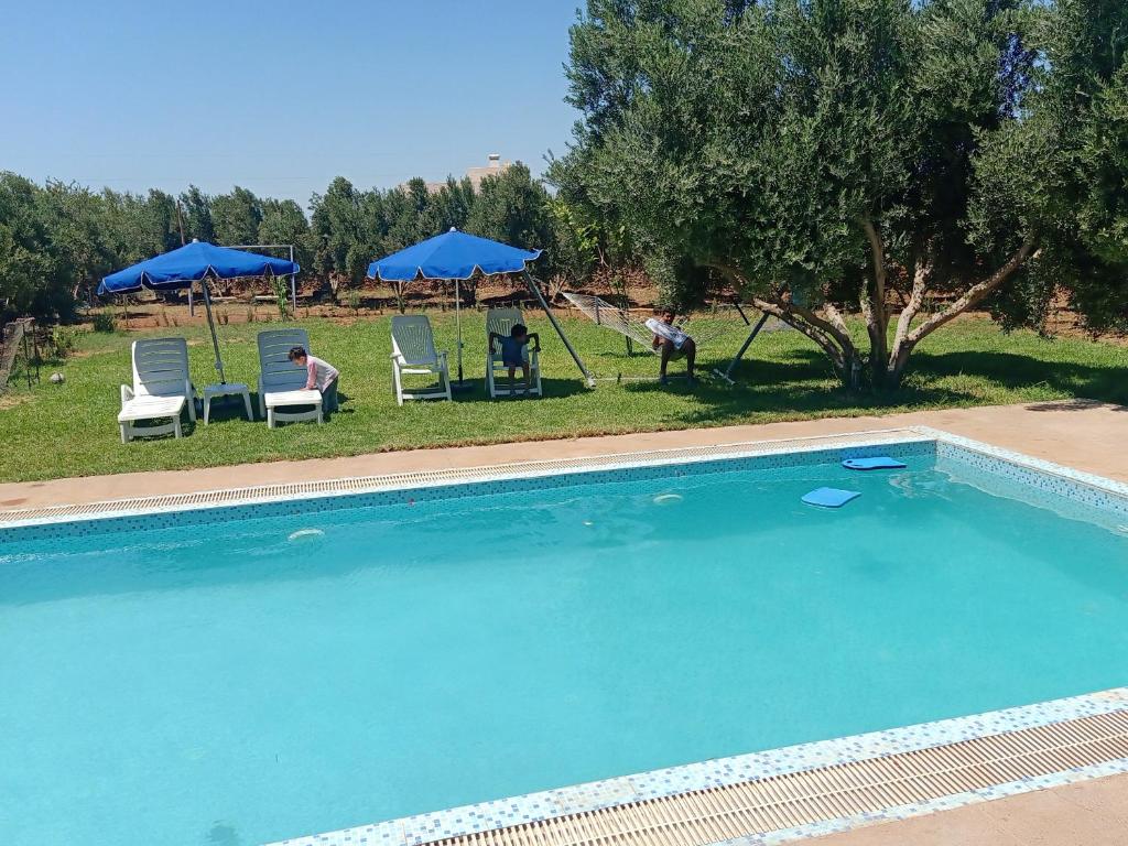 a swimming pool with two people in chairs and umbrellas at Jardin de rayane in Essaouira