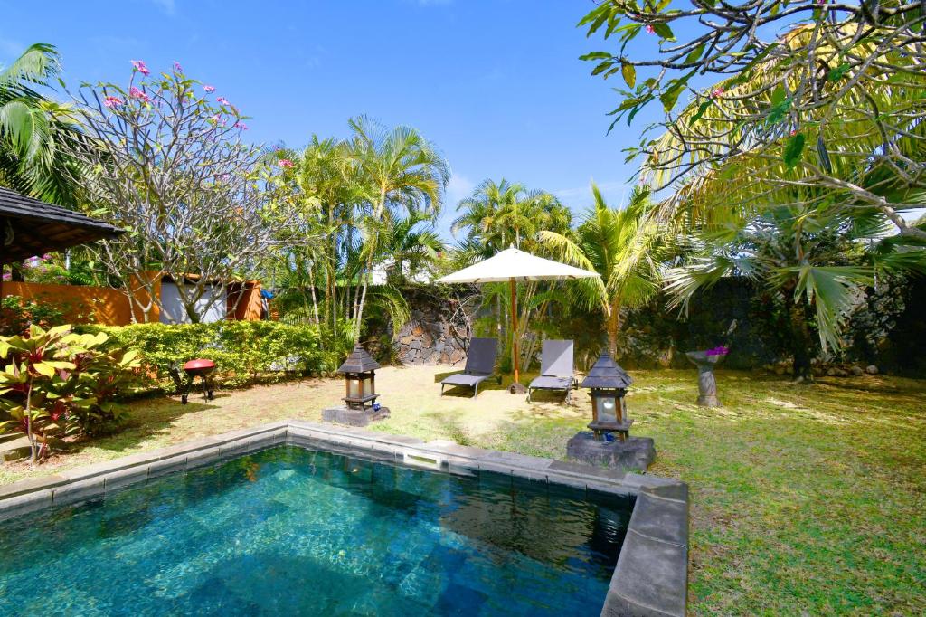 a swimming pool in a yard with two chairs and an umbrella at Elegant Villa Bali style in Blue Bay in Blue Bay