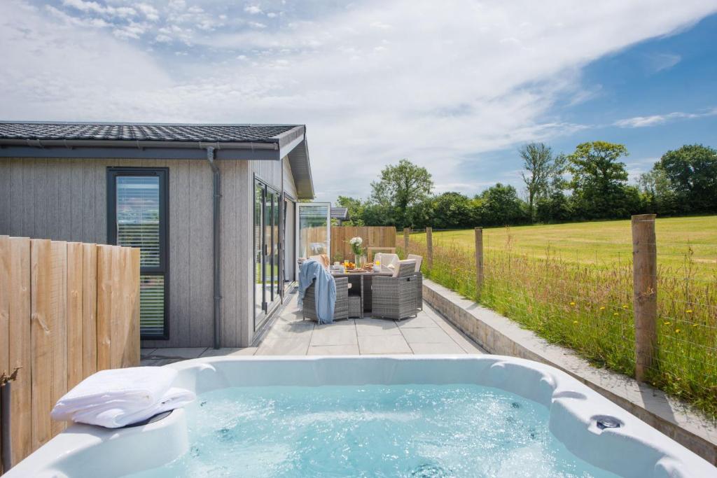 einen Whirlpool auf einer Terrasse mit einem Tisch und Stühlen in der Unterkunft Lavender Lodge, 8 Roadford Lake Lodges in Lifton