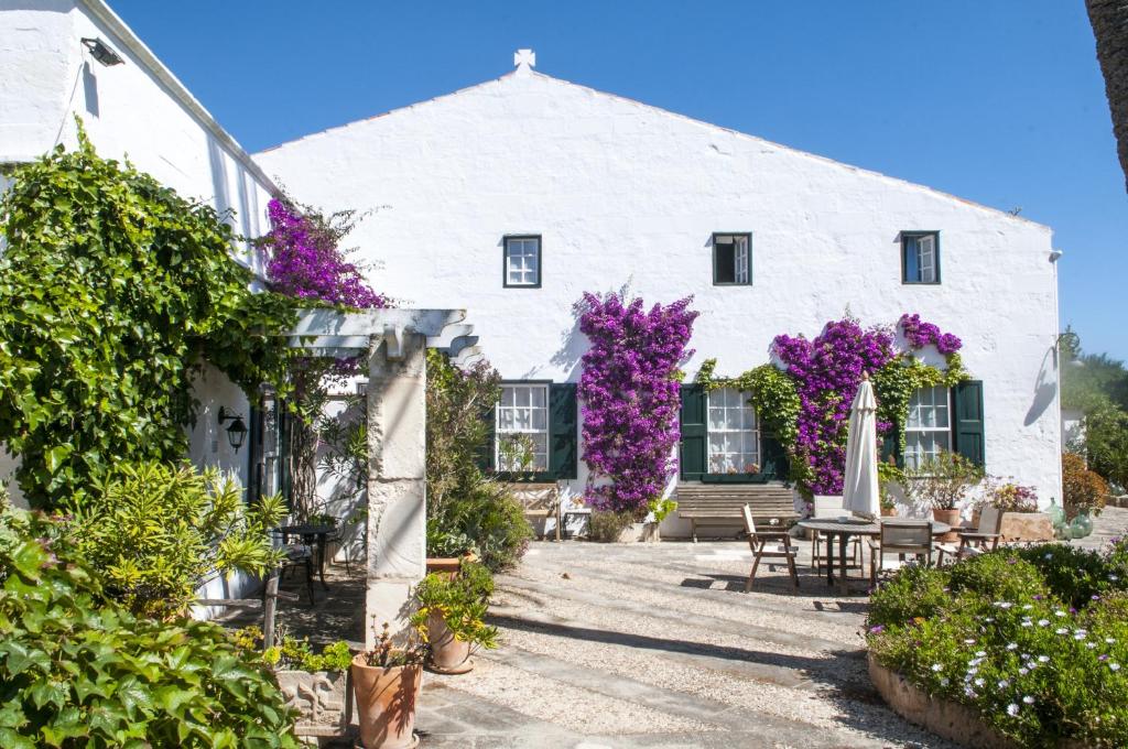 Una casa blanca con flores púrpuras. en Hotel Rural Biniarroca - Adults Only, en Sant Lluis