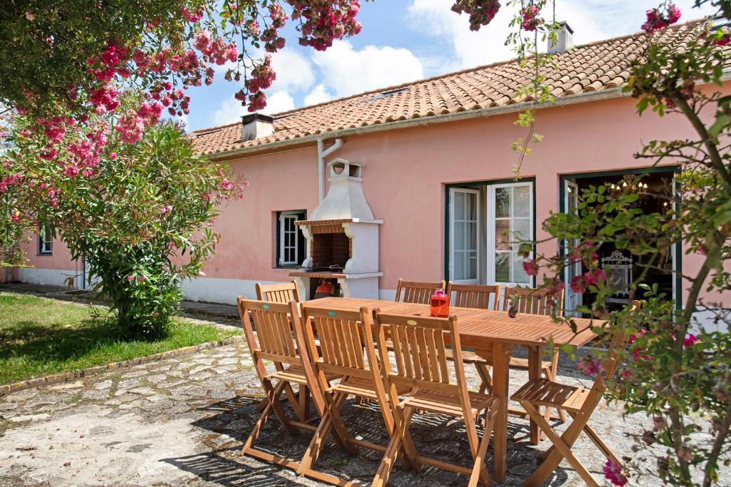 a wooden table and chairs in front of a pink house at Casa Alfeizerão in Alfeizerão