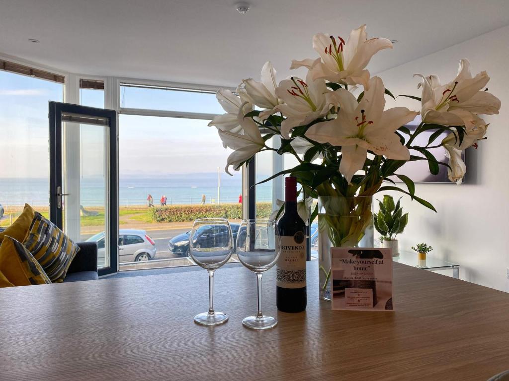 a bottle of wine and two glasses on a table with flowers at Eden Escapes Serviced Apartments in Morecambe
