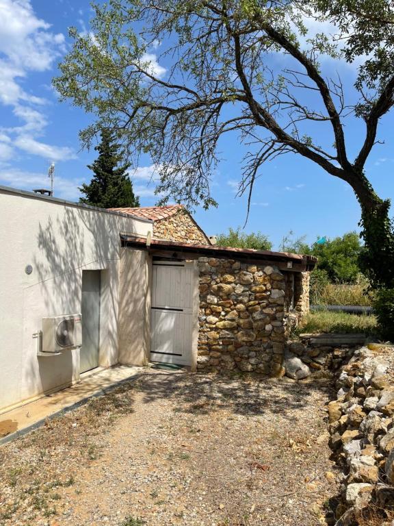 um edifício de pedra com uma garagem e uma árvore em Le Fenouillet Cottage proche des Grands Buffets em Narbona