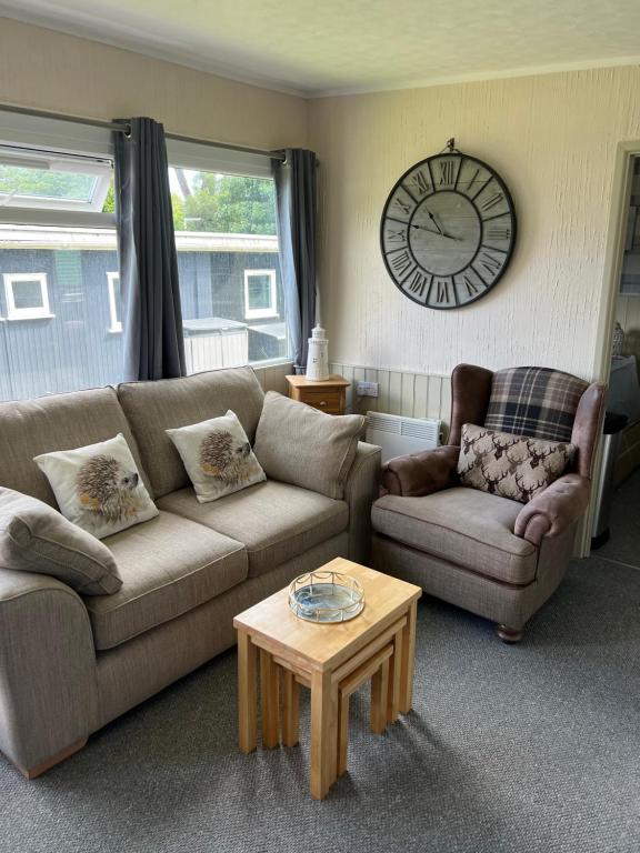 a living room with a couch and a table and a clock at Woodlands Hedgehog Chalet, Bideford Bay Holiday Park in Bucks Mills