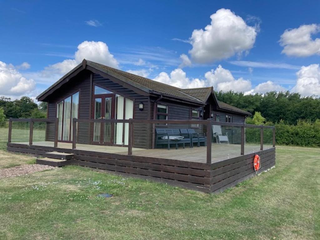 une grande cabine en bois avec une terrasse dans un champ dans l'établissement Lakeside cabin set in the Kentish countryside, à Bethersden
