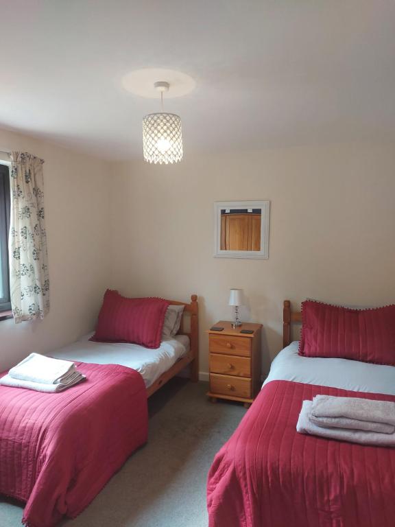 a bedroom with two beds with red sheets and a dresser at 10 The Parklands - Cosy Bungalow in Cornwall in Kilkhampton