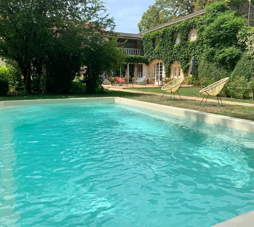 a swimming pool with two chairs in front of a house at Clos de la Court d'Aron in Saint-Cyr-en-Talmondais