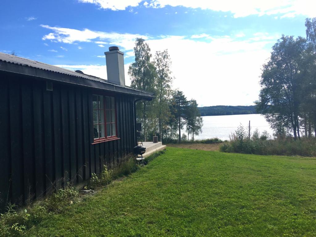 a black house with a grass yard next to a lake at Nærglimt - cabin by the lake Næra in Ringsaker