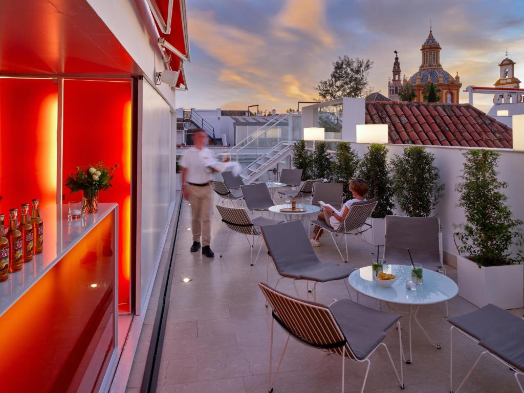 un uomo in piedi su un balcone con tavoli e sedie di Hotel Rey Alfonso X a Siviglia