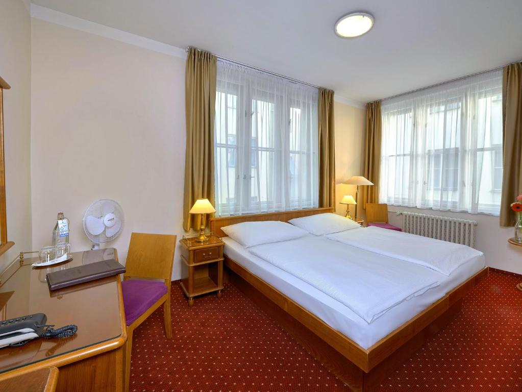 een slaapkamer met een groot wit bed en ramen bij Hotel Melantrich in Praag