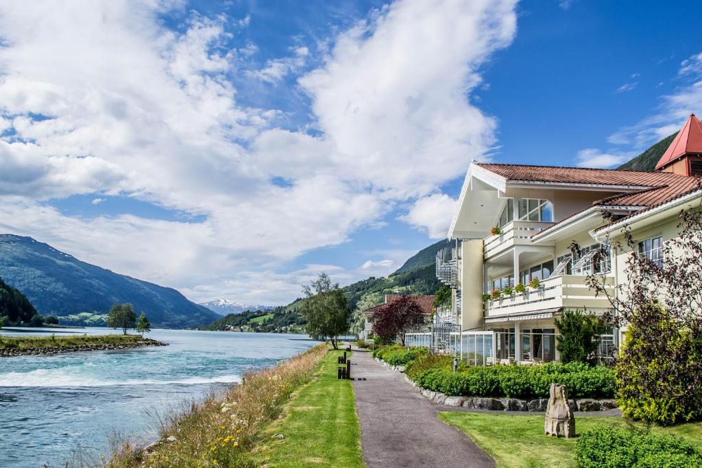 a building next to a river with mountains at Hotel Loenfjord Loen in Loen