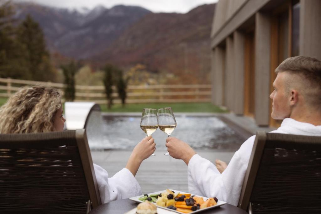 a man and woman sitting at a table with glasses of wine at Hotel Bohinj in Bohinj
