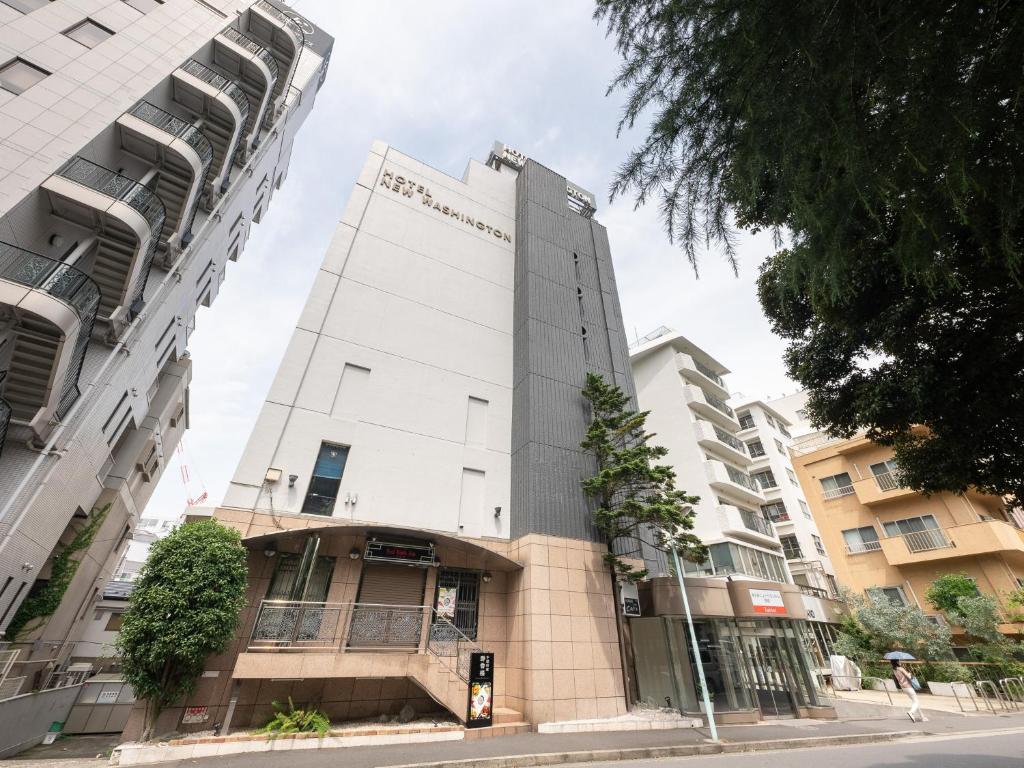 a tall white building on a street with buildings at Tabist Hotel New Washington Shibuya in Tokyo