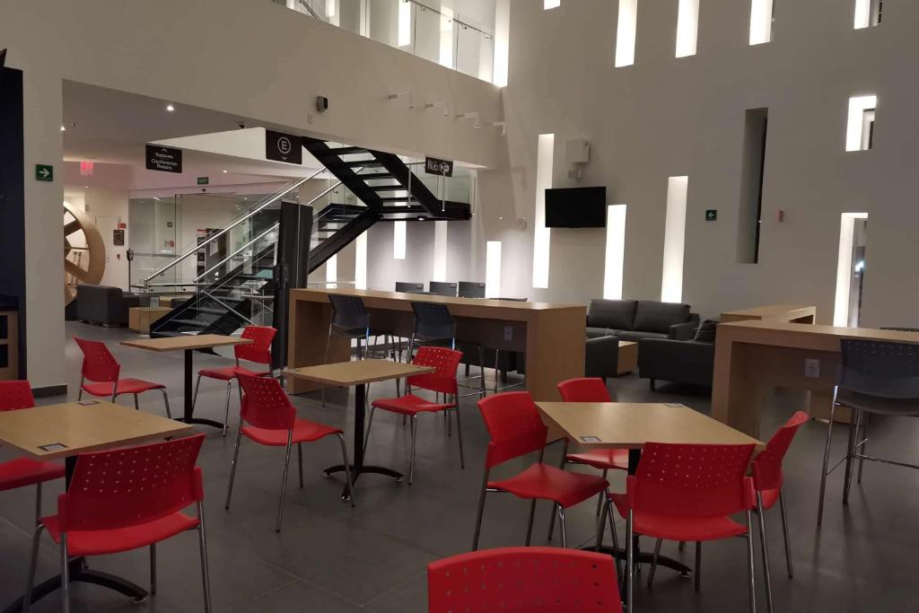 a restaurant with red chairs and tables and a staircase at Ramada Encore by Wyndham Guadalajara Aeropuerto in Guadalajara