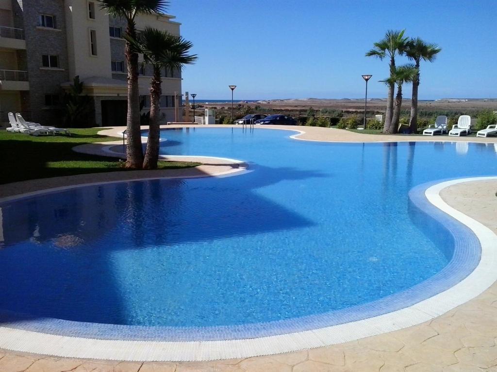 a large blue swimming pool with palm trees and a building at Appartement Bella Vista in Bouznika