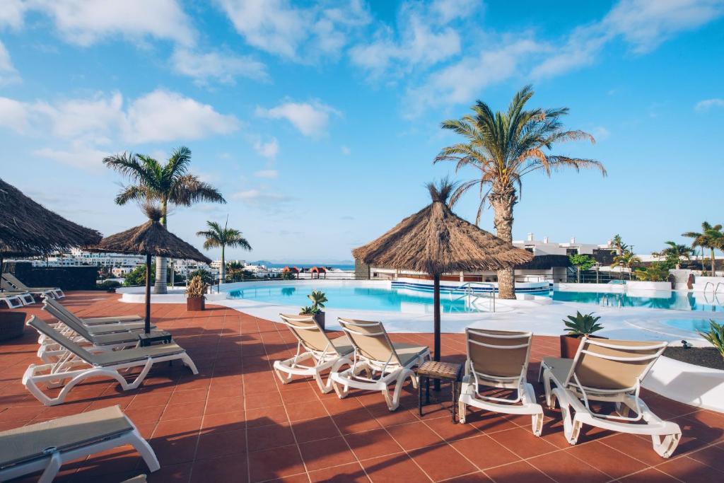 a resort pool with chairs and palm trees at Dreamplace Bocayna Village in Playa Blanca