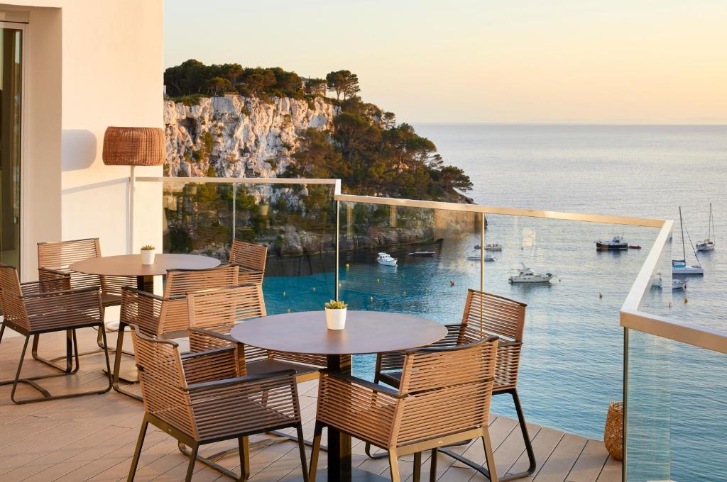 a balcony with tables and chairs and a view of the ocean at Meliá Cala Galdana in Cala Galdana