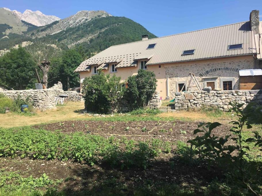 a house with a stone wall and mountains in the background at Très Grand Gîte équipé à la montagne in Le Glaizil