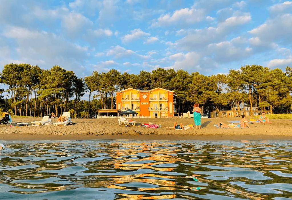 a group of people on a beach with a yellow house at Sea Line Hotel in Shekvetili